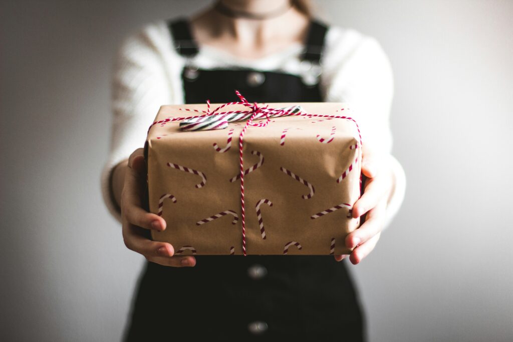 Woman holding out wrapped gift as an representation of gift-giving to grandkids, and as one answer to "how to leave grandkids your retirement savings"