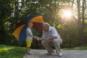 Grandfather holding umbrella for grandson to represent the importance of writing up a legacy plan for your family