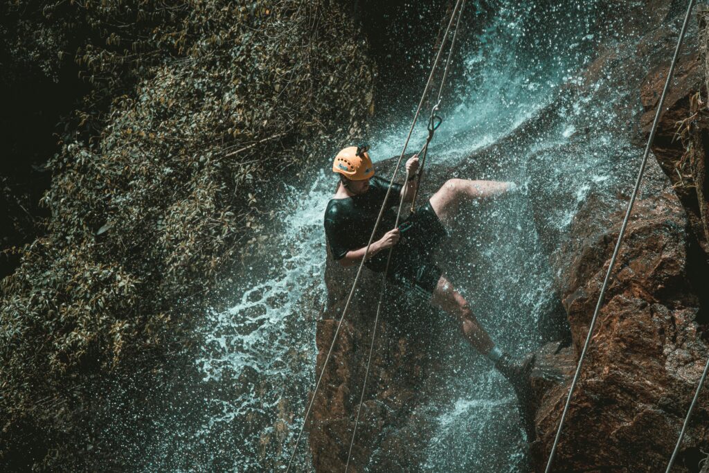 A person wearing safety gear and engaging in risky behavior by trying to rock climb with water gushing down on them, to illustrate the importance of risk management.