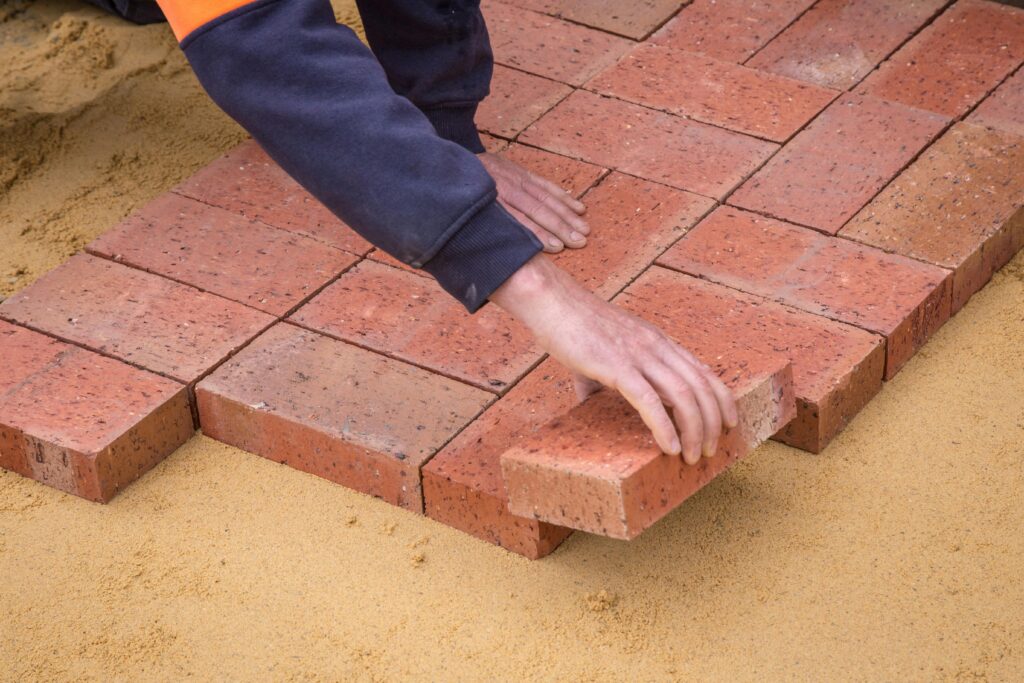 A person is laying red bricks on leveled sand, demonstrating how you have to actively build your wealth.