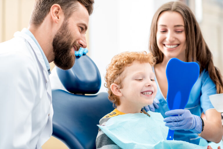 A dentist and hygienist show a little boy his teeth in a mirror.